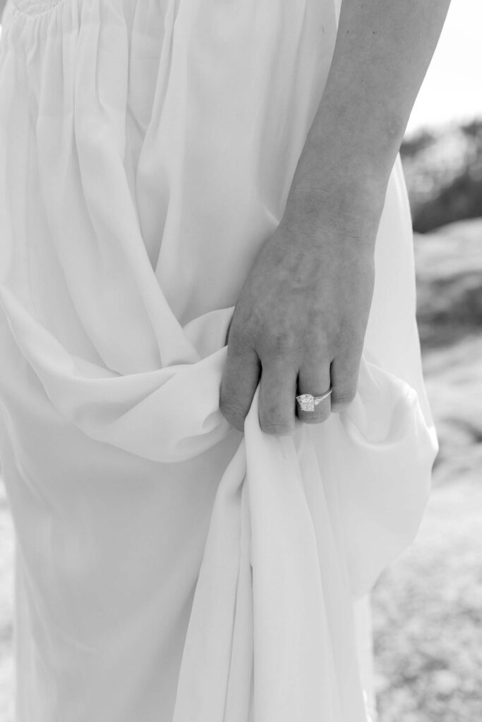 Close up of engagement ring on woman's finger while holding her dress in Emerald Bay