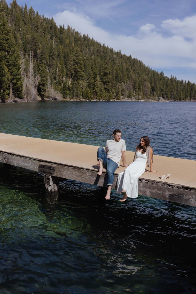 Engagement couple sitting and relaxing on pier together surrounded by Lake Tahoe with forest of pine trees in background at Emerald Bay