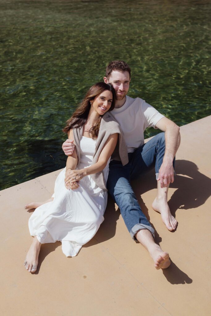 Engagement couple sitting on a pier together in Emerald Bay while smiling at the camera