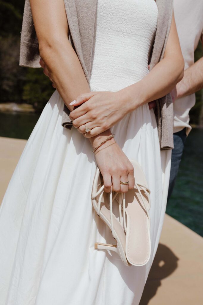Close up of engagement couple standing on pier while woman holds shoes and has engagement ring on finger in Emerald Bay