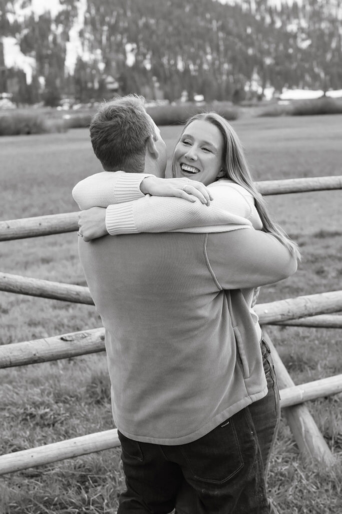Engagement couple hugging while woman is smiling with wooden fence and snowy mountains in background at Palisades