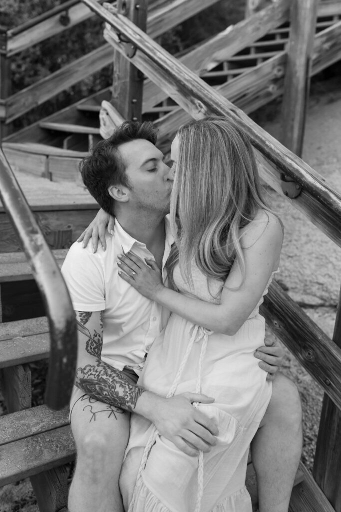 Engagement couple sitting together on wooden staircase while kissing on a beach in Lake Tahoe