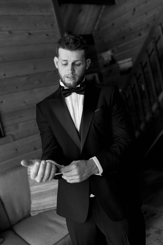 Wedding groom adjusting cufflinks with wooden walls in background at Garwoods in Lake Tahoe