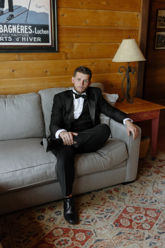 Groom sitting on couch with legs crouched looking at camera with wooden wall behind him at Garwoods Lake Tahoe