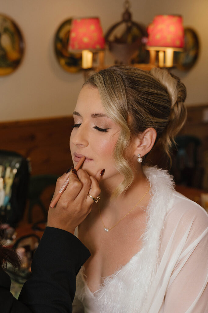 Bride with her eyes closed while makeup artist applies makeup to her with yellow lights in background at Garwoods Lake Tahoe