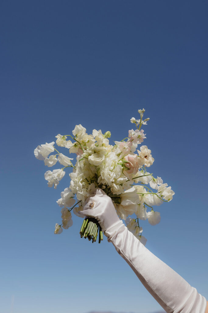 Bride holding her floral bouquet in the air with sky in background at Garwoods in Lake Tahoe