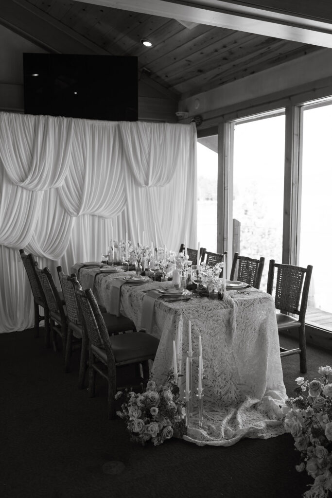 Wedding dinner table with long white tablecloth next to tall windows with silky wall in background at Garwoods in Lake Tahoe