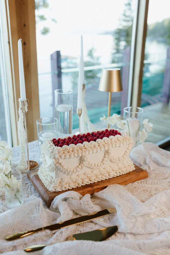White wedding cake with raspberries sitting on wooden plate next to white florals and golden cutlery at Garwoods Lake Tahoe