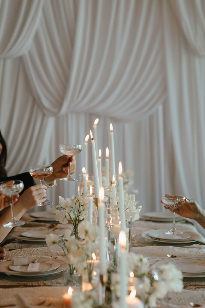 Lit candles in a row on wedding table while guests hold drinks with silky curtains in background at Garwoods at Lake Tahoe
