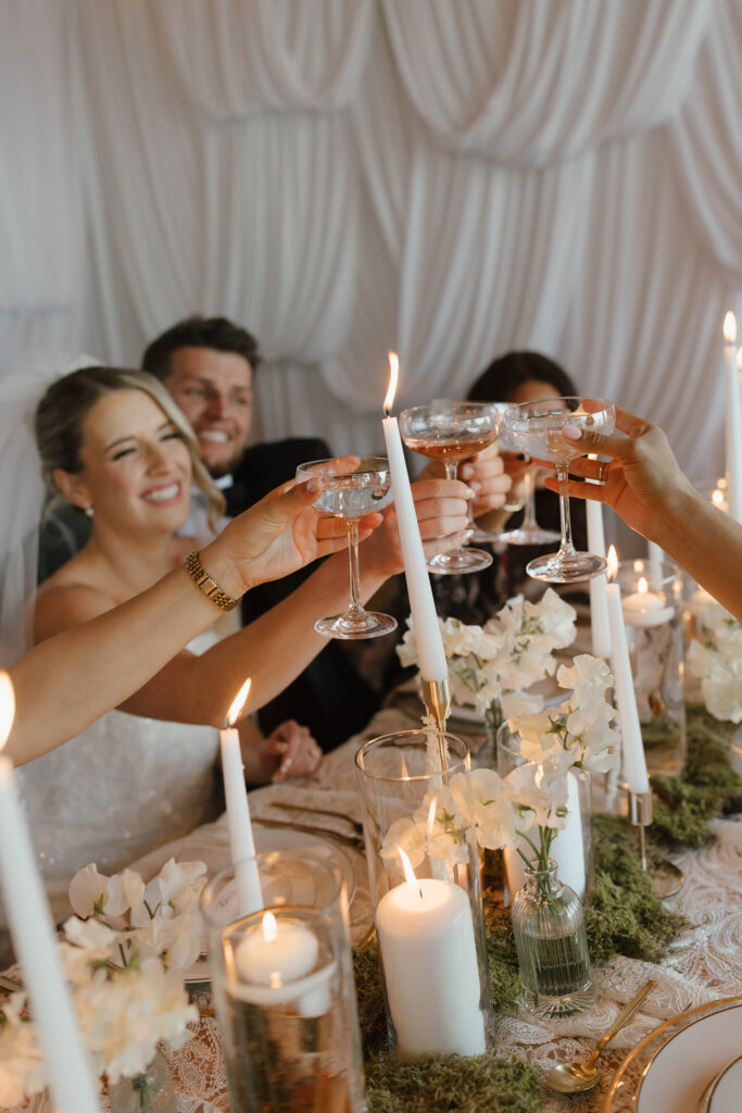Wedding couple sitting at dinner table and smiling while cheering drinks with guests over white florals at Garwoods at Lake Tahoe