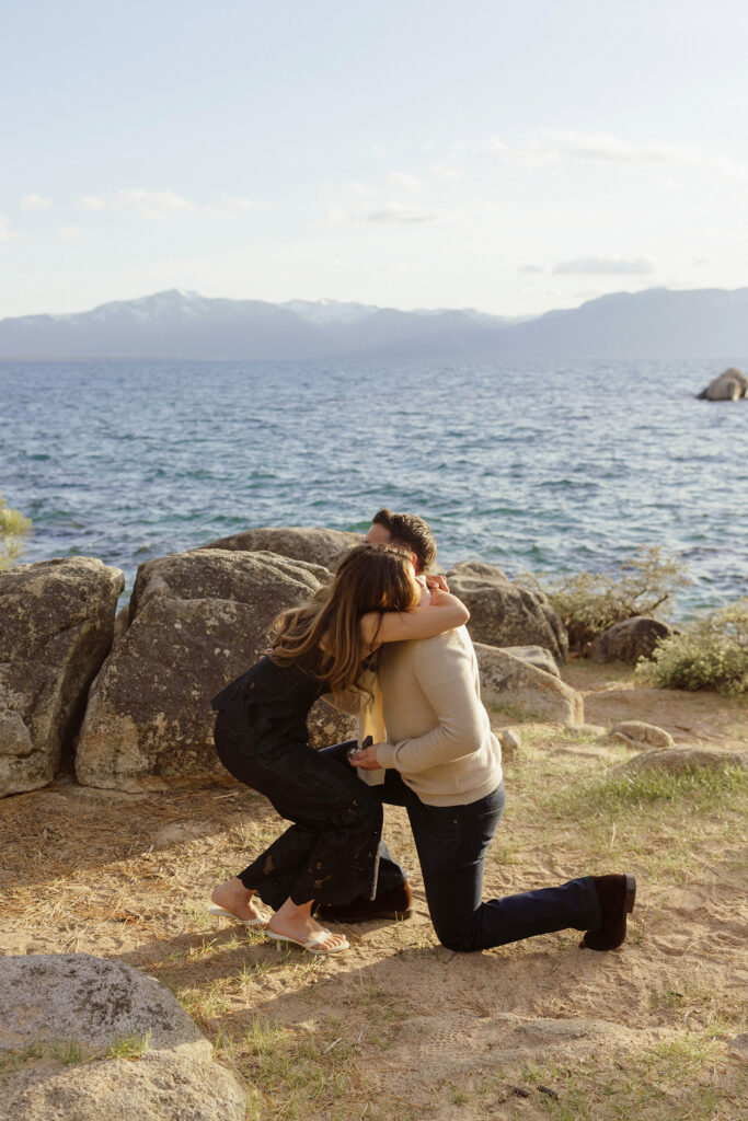 Woman hugging fiancé on one knee after proposal in Zephyr Cove with Lake Tahoe in background