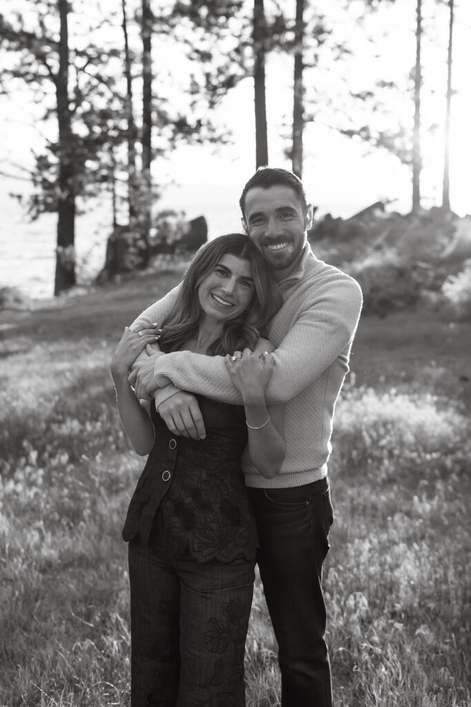 Engagement couple holding each other while smiling at camera with pine trees in background at Zephyr Cove