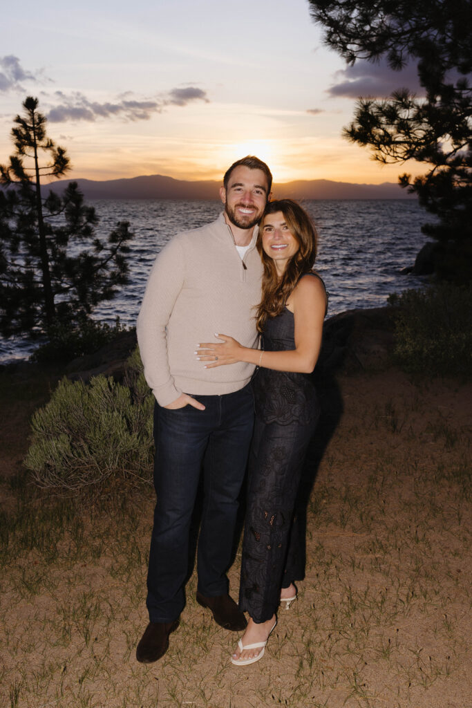 Engagement couple holding each other while smiling at camera with sunset in background at Zephyr Cove