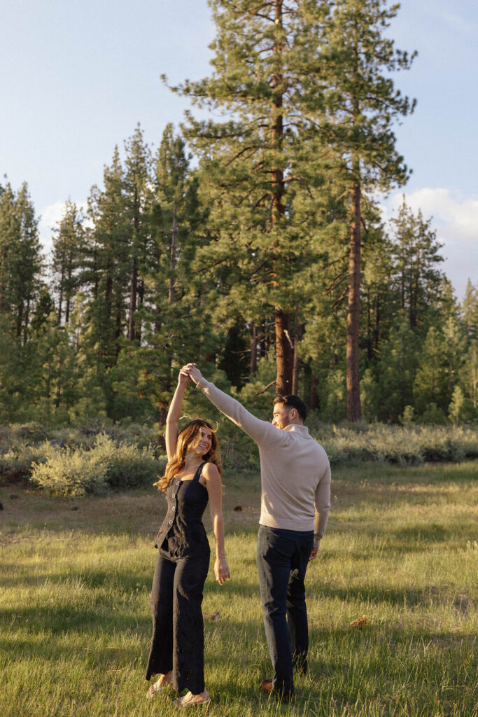 Man spinning fiancé around while in a open field together with pine trees in background at Zephyr Cove