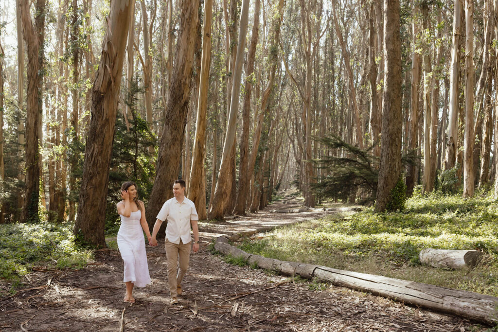 Couple walking through Lovers' Lane during a San Francisco engagement session surrounded by towering eucalyptus trees