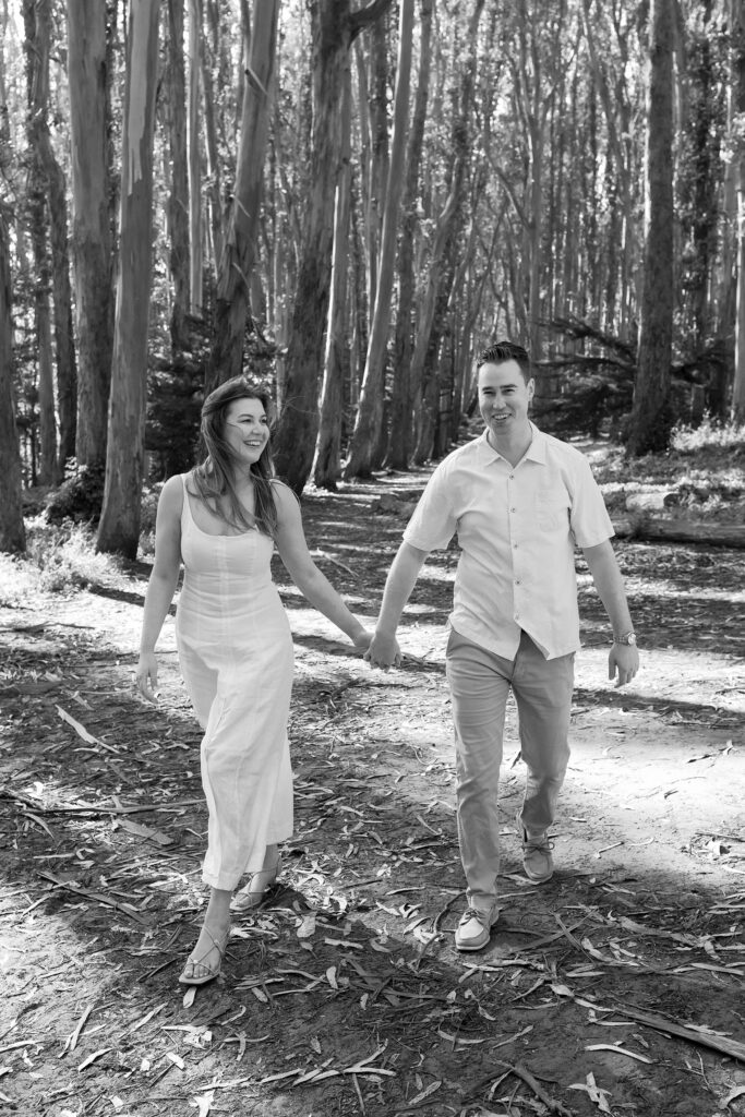 Black and white photo of an engaged couple holding hands while walking through the forest at Lovers' Lane in San Francisco