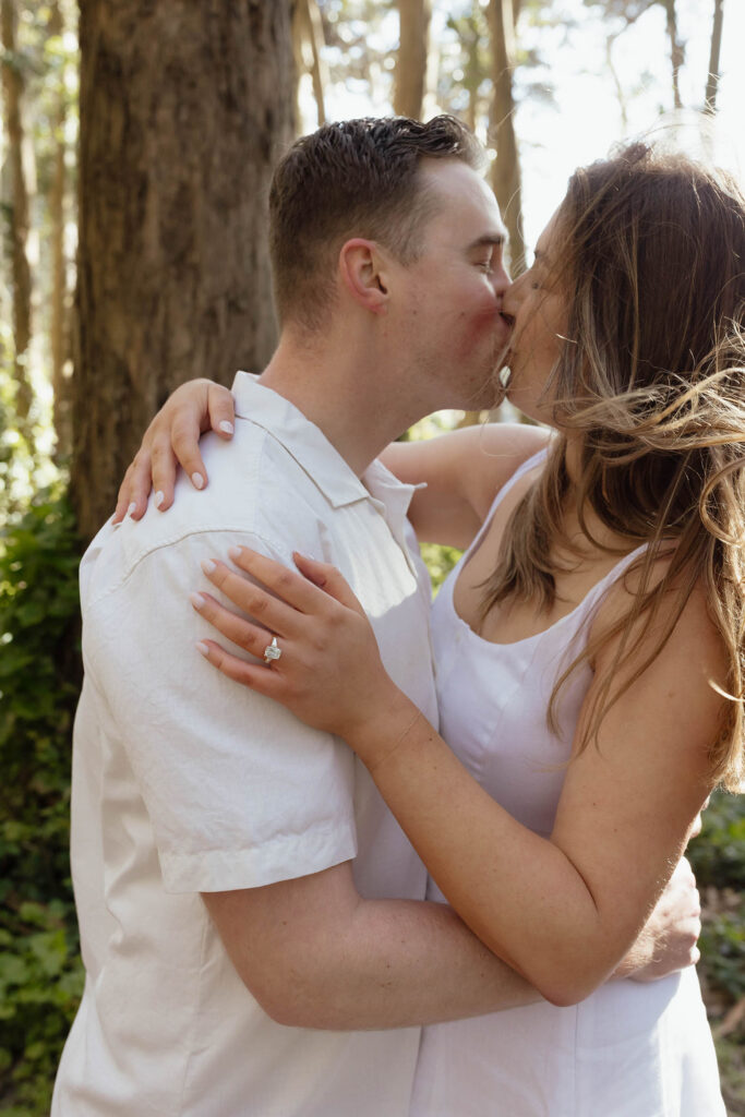 Engaged couple sharing a kiss beneath the trees at Lovers' Lane during their San Francisco engagement session, with the engagement ring visible