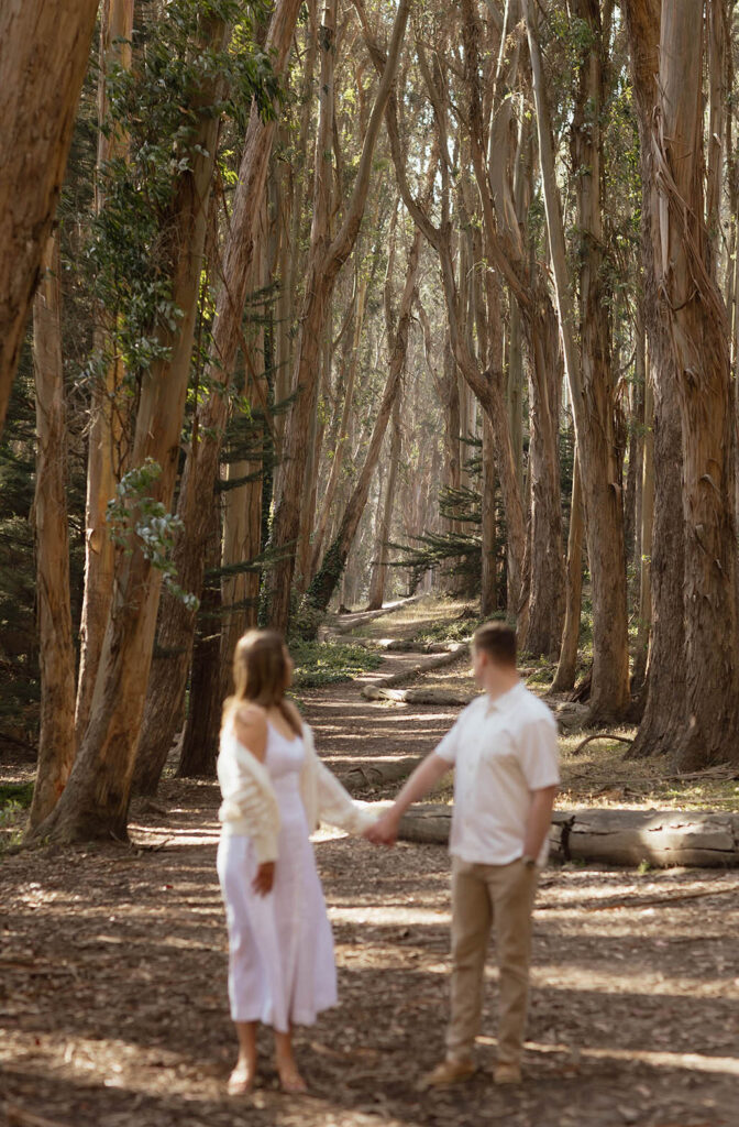 Engaged couple holding hands looking back at the trees at Lovers' Lane during their San Francisco engagement session