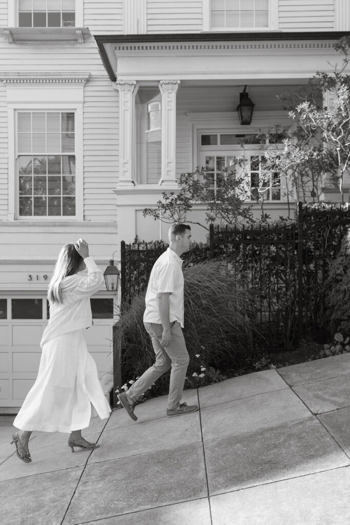 Black and white photo of an engaged couple walking through the city of San Fransisco while woman puts her hand through her hair
