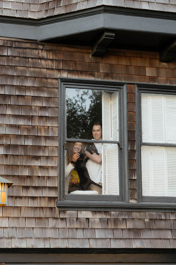 Engaged couple holding their cats inside an apartment in San Fransisco looking through the window and smiling