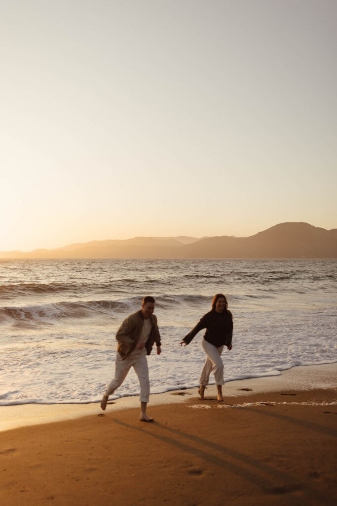 Couple running on the beach at sunset in San Fransisco with the water in focus