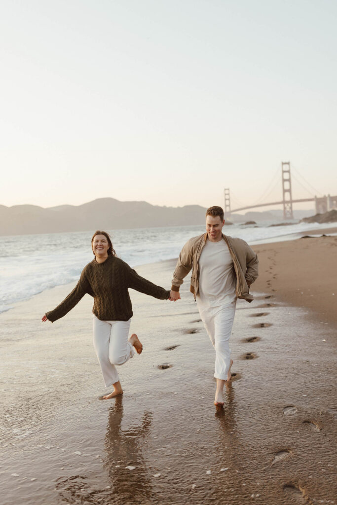 Engaged couple running on the beach at sunset with the Golden Gate bridge in the background