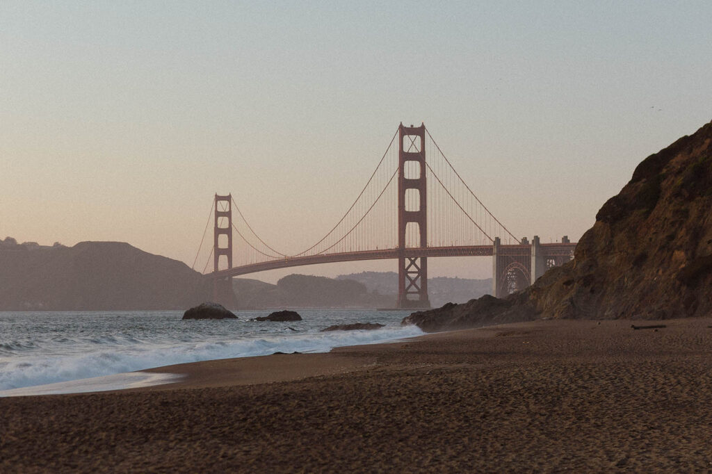 Sunset photo of the golden gate bridge in San Fransisco with the ocean and mountains in view