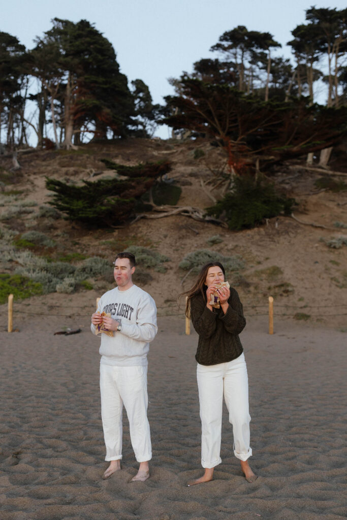 Couple eating taco bell on the beach in San Fransisco barefoot with the mountains and trees in the background