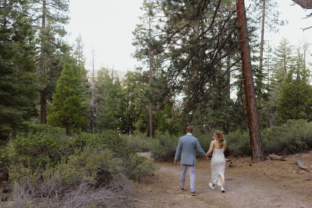 Elopement couple holding hands and walking along dirt trail together through pine trees in Lake Tahoe