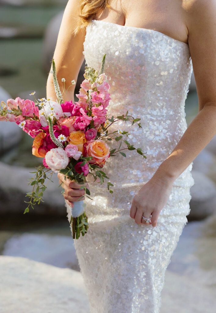 Close up of bride holding colorful floral bouquet next to sparkly wedding dress at Lake Tahoe