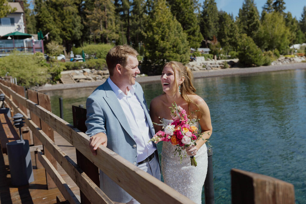 Elopement couple laughing while standing on a pier together at Lake Tahoe with lake and pine trees in background
