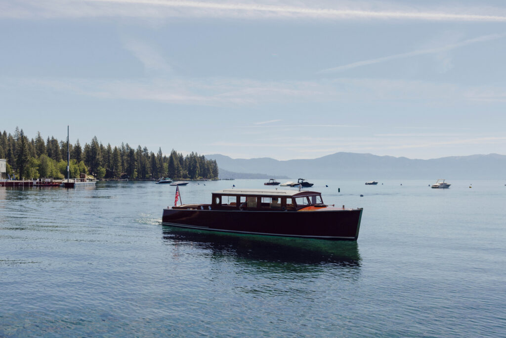Wooden boat driving across Lake Tahoe with pine trees and mountains in background