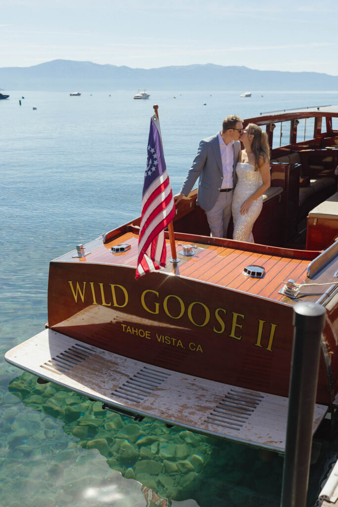 Elopement couple kissing while standing on wooden boat together on Lake Tahoe with mountains in background