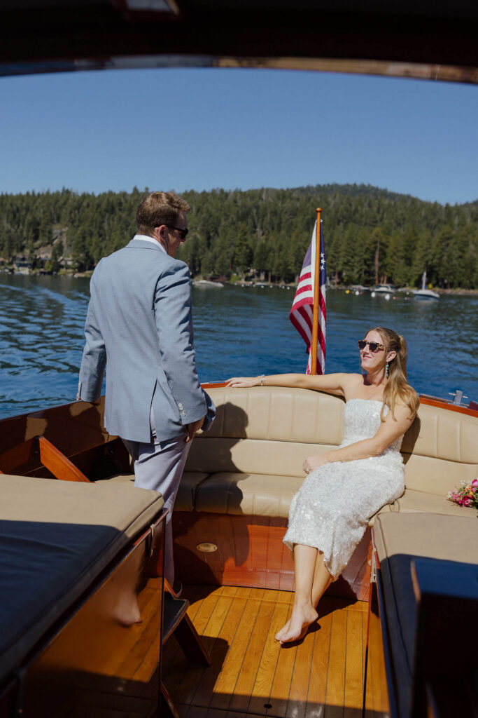 Groom with hand in his pocket standing and talking to bride sitting on couch on back of the boat while they ride out on Lake Tahoe