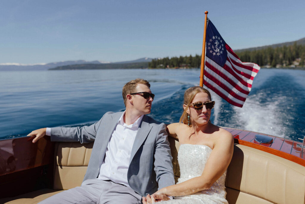 Elopement couple sitting on boat together holding hands while riding across Lake Tahoe with flag flapping behind them