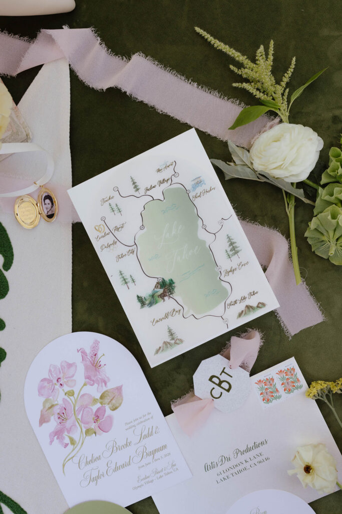 Wedding announcements and details in flatlay with white roses on green tablecloth at Everline Resort in Lake Tahoe