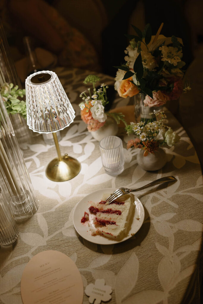 Close up of cake on a plate on wedding reception table next to light and floral bouquets at Everline Resort in Lake Tahoe