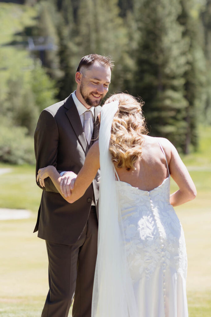 Groom smiling while holding bride's arm in open field at Everline resort at Lake Tahoe with pine trees in background