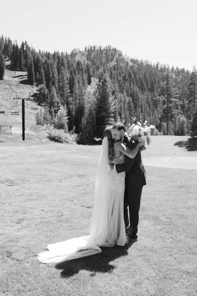 Wedding bride and groom's first look in open grass field with mountains and pine trees in background while hugging at Everline Resort at Lake Tahoe