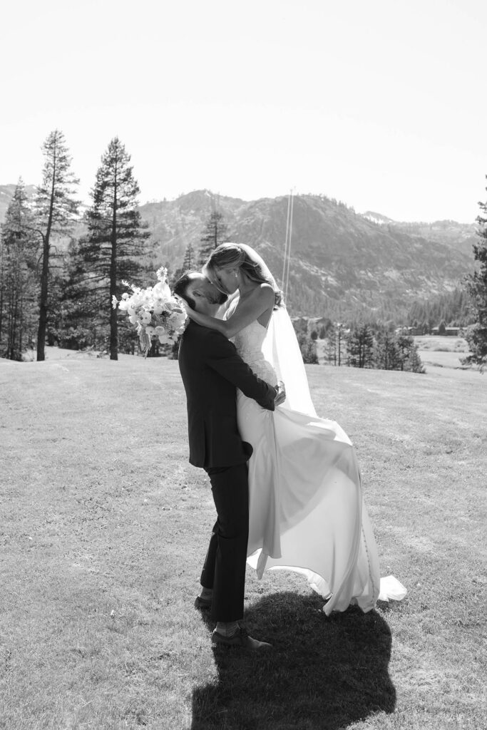 Wedding groom lifting up bride while they kiss and she holds floral bouquet in open field at Everline Resort in Lake Tahoe