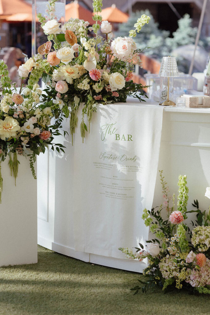 Wedding bar menu sign draped over white wall next to colorful floral bouquets at Everline Resort at Lake Tahoe