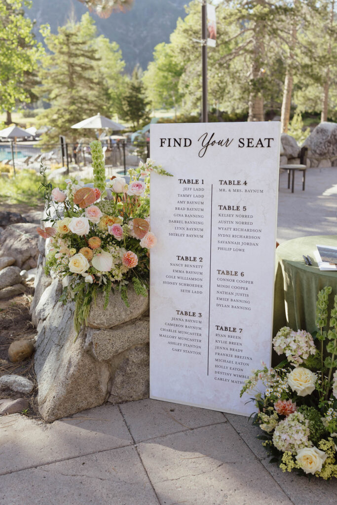 Wedding dinner table seating chart sign next to rock wall and colorful floral bouquets at Everline Resort at Lake Tahoe