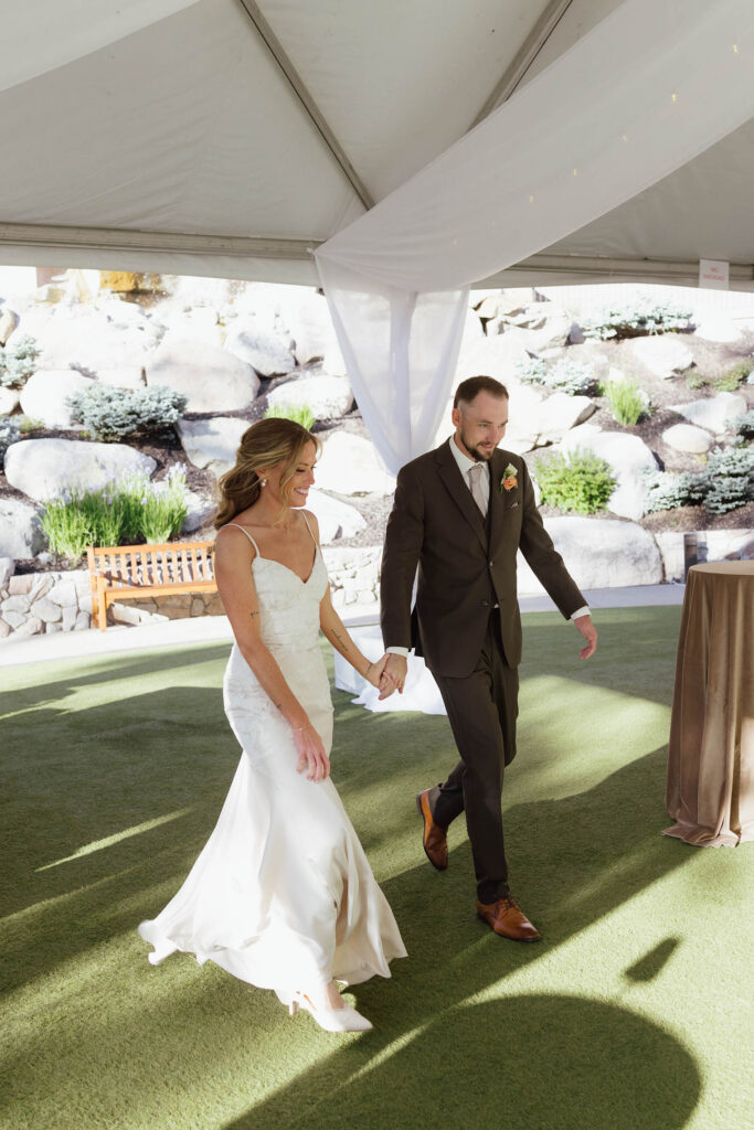 Wedding couple holding hands while walking into reception together underneath white canopy at Everline Resort in Lake Tahoe