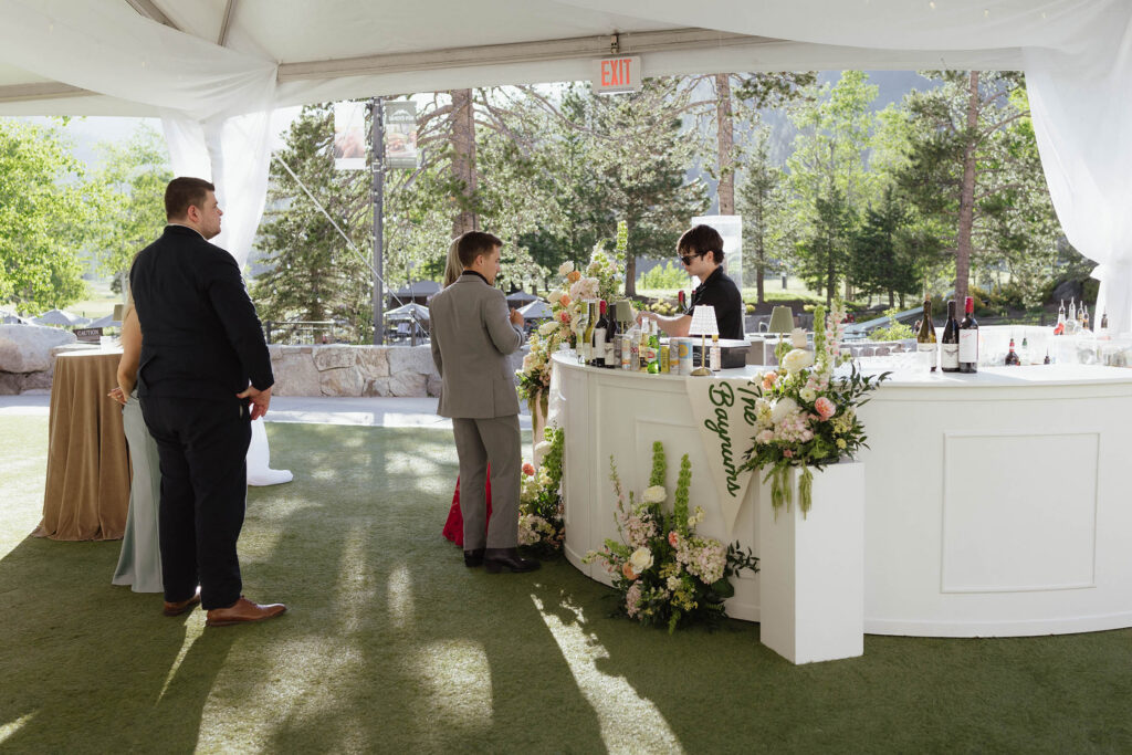 Wedding guests ordering drinks from bar decorated in colorful florals during reception at Everline Resort at Lake Tahoe