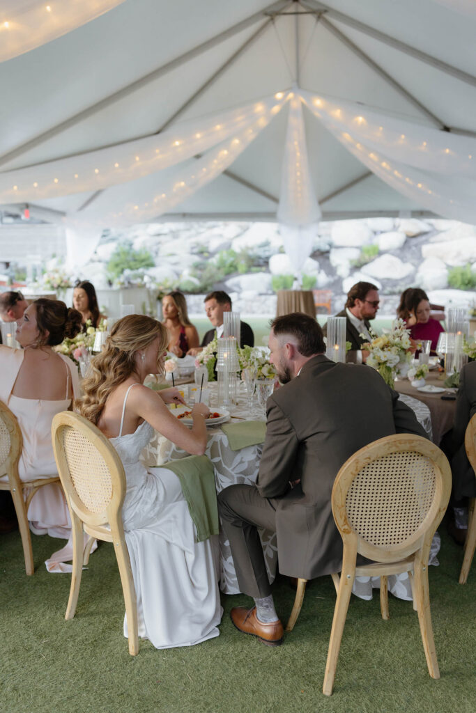 Wedding couple sitting together at table during reception underneath string lights and large gazebo at Everline Resort in Lake Tahoe