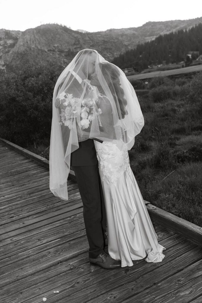 Wedding couple kissing while covered by bride's veil on wooden walkway at Everline Resort in Lake Tahoe