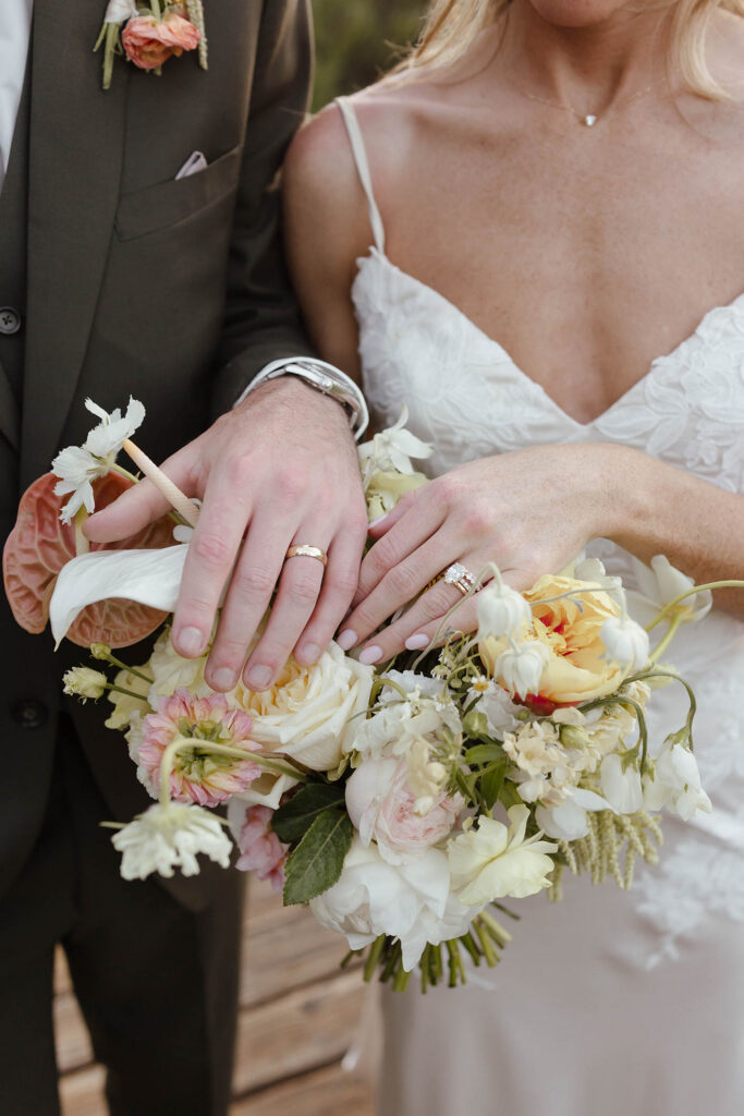 Close up of wedding couple's hands wearing wedding rings on top of floral bouquet at Everline Resort in Lake Tahoe
