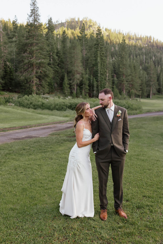 Bride leaning on Groom's shoulder while they smile at each other in an open field in Everline Resort at Lake Tahoe with forest of pine trees in background