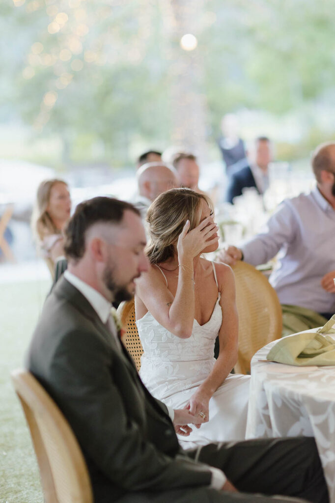 Bride emotional and wiping tears while listening to speeches and holding Groom's hand during reception at Everline Resort in Lake Tahoe