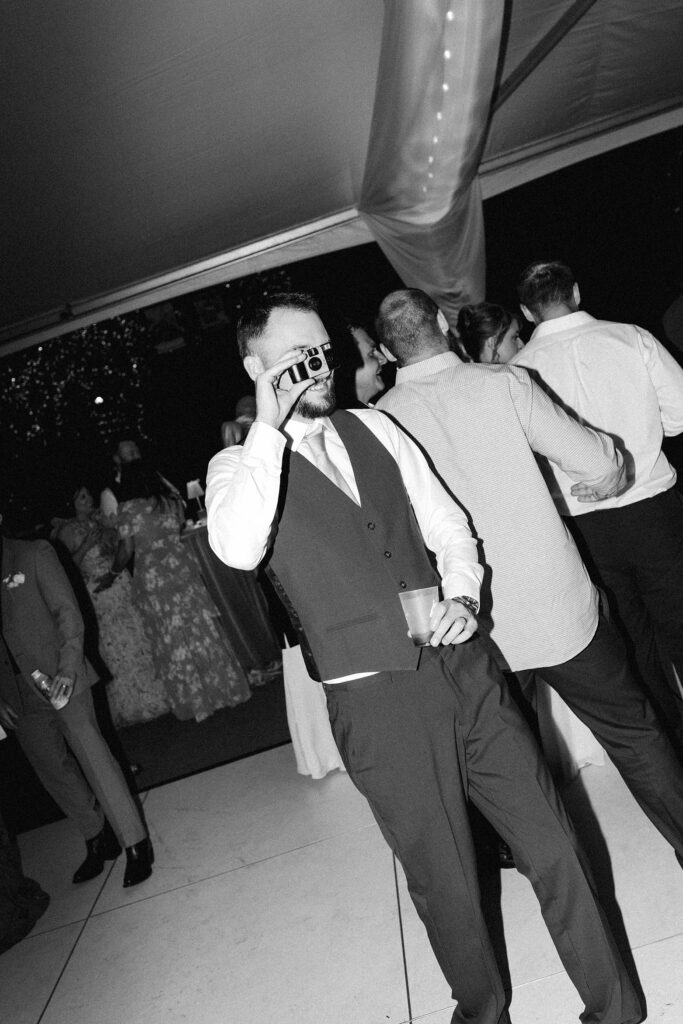 Groom using disposable camera while holding a drink during wedding reception at Everline Resort in Lake Tahoe